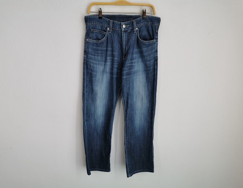 May include: Blue denim jeans hanging on a wooden hanger. The jeans have a classic five-pocket design, a button and zip closure, and a medium wash. The denim trousers are a straight-leg style.