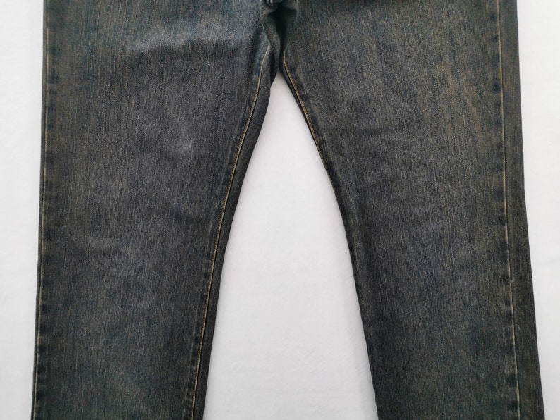 May include: Close-up of faded black denim jeans. The jeans have a classic five-pocket design and a straight leg cut. The stitching is a contrasting yellow-gold colour.