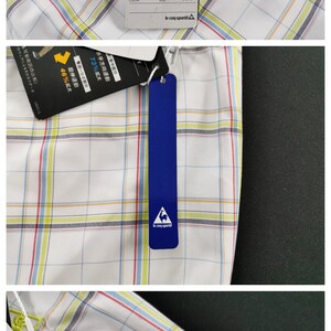 Op de afbeelding: Een wit golf shirt met een blauw, rood en geel ruitpatroon. Het shirt heeft een label met de tekst "Blue Line" en "We Sell Functions Cool but Real 100% le coq sportif Golf Collection".