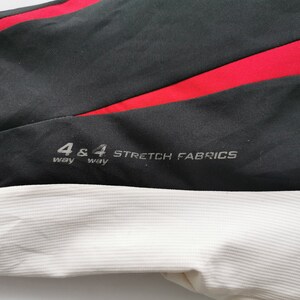 Pode incluir: Close-up de tecido preto com uma faixa vermelha e tecido branco canelado. O texto "4 & 4 way STRETCH FABRICS" est&aacute; impresso no tecido preto. A imagem mostra uma se&ccedil;&atilde;o de roupa esportiva ou tecido de desempenho.