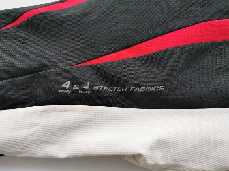 Pode incluir: Close-up de tecido preto com uma faixa vermelha e tecido branco canelado. O texto "4 & 4 way STRETCH FABRICS" est&aacute; impresso no tecido preto. A imagem mostra uma se&ccedil;&atilde;o de roupa esportiva ou tecido de desempenho.