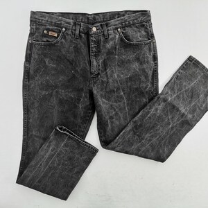 May include: Acid wash black denim jeans. The jeans have a classic five-pocket design, a button and zipper closure, and a small logo patch on the front pocket. The denim has a faded, distressed look.