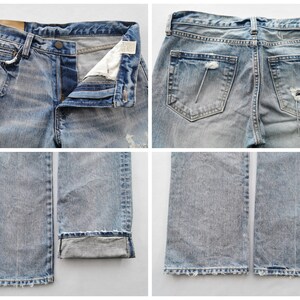 May include: Light blue denim jeans with distressed details, including rips and fading. The jeans have a button fly, classic five-pocket design, and a slightly worn appearance. The bottom of the jeans are cuffed.