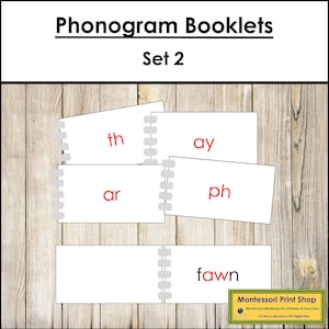 May include: White phonogram booklets with red text spelling out "th", "ay", "ar", "ph", and "fawn". The booklets are arranged on a wooden background. The text "Phonogram Booklets Set 2" is at the top.