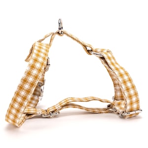 May include: A dog harness featuring a yellow and white check pattern. It has a metal D-ring for lead attachment and adjustable straps with metal buckles. The harness is designed for small to medium-sized dogs.