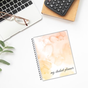 May include: A spiral bound student planner with a watercolor background in shades of orange and yellow. The text "my student planner" is printed in black on the front cover.