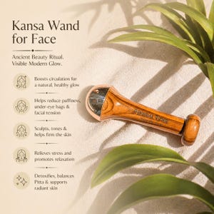May include: A Kansa wand for the face, made of wood and metal, lies on a sandy surface with green foliage. The wand has a rounded metal end and the text "HERBAL EDGE" is visible. Text on the left describes the wand's benefits.