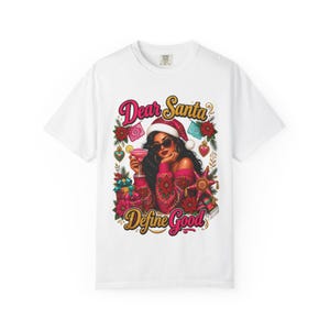 Könnte beinhalten: Ein weißes T-Shirt mit einer Grafik einer Person, die eine Weihnachtsmütze und eine Sonnenbrille trägt und einen rosa Cocktail hält. Das Design zeigt Geschenke, Weihnachtssterne und den Text "Dear Santa Define Good".