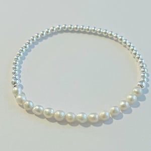 May include: A silver and white beaded bracelet with a half circle of silver beads and a half circle of white pearls.