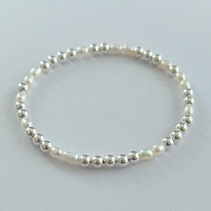 May include: A silver bracelet with small silver beads and white pearl beads.