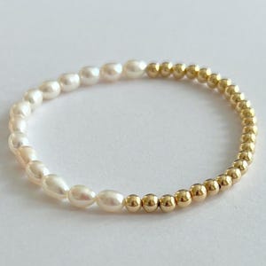 May include: A delicate bracelet featuring a combination of creamy white freshwater pearls and small, round gold beads. The pearls are on one side, transitioning to the gold beads on the other. The bracelet is on a white background.