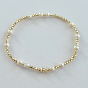 May include: A delicate gold bracelet with small white pearls. The bracelet is made of tiny gold beads and features a single larger gold bead in the center.