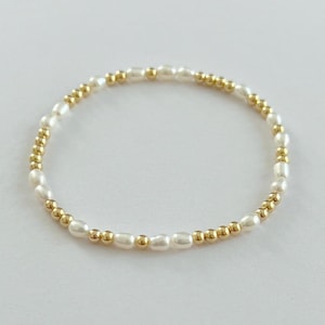 May include: A delicate bracelet made of small gold beads and white pearls. The bracelet is simple and elegant, perfect for everyday wear.