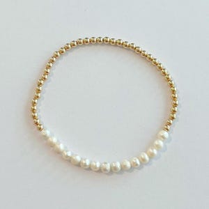 May include: A gold and white beaded bracelet with a row of white pearls.