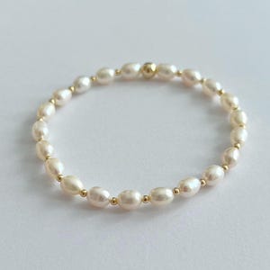 May include: An elegant bracelet featuring creamy white oval pearls strung together with small gold-colored beads. The bracelet is a delicate piece of jewelry, perfect for adding a touch of sophistication to any outfit.