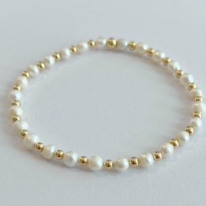 May include: A delicate bracelet made of small white pearls and gold beads. The bracelet is simple and elegant, perfect for everyday wear.