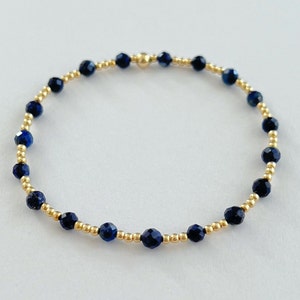 May include: A delicate gold bracelet with small blue beads. The bracelet is made of tiny gold beads and dark blue gemstone beads.