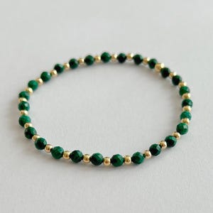 May include: A green malachite and gold bead bracelet. The bracelet is made with small, round beads that are strung together on a thin gold chain.