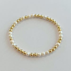 May include: A gold and white beaded bracelet with alternating gold and white beads.