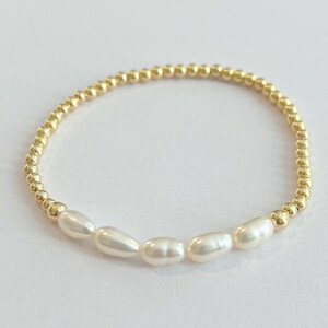 May include: A delicate gold beaded bracelet with a row of white freshwater pearls.