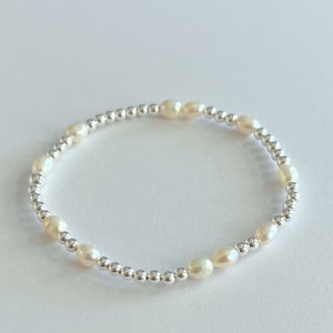 Pode incluir: Um bracelete delicado feito com pequenas contas prateadas e pérolas brancas.