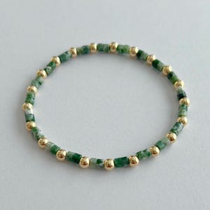 Könnte beinhalten: Ein grünes und goldenes Armband. Das Armband besteht aus kleinen, quadratischen grünen Perlen und runden goldenen Perlen.