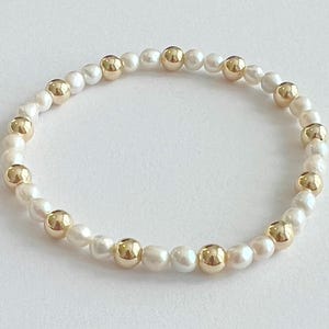 May include: A bracelet made of white pearls and gold beads. The bracelet is made of a string of alternating white pearls and gold beads.