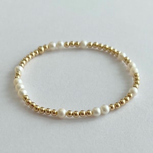 May include: A delicate bracelet featuring alternating white pearls and gold-colored beads. The bracelet is circular and appears to be made of small, round beads strung together. The pearls are a creamy white color, and the gold beads add a touch of elegance.