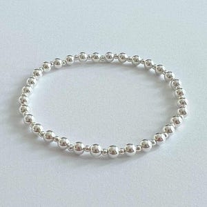 May include: A silver beaded bracelet. The bracelet is composed of small, round, shiny silver beads strung together to form a complete circle. The beads are uniform in size and evenly spaced, creating a simple and elegant design.