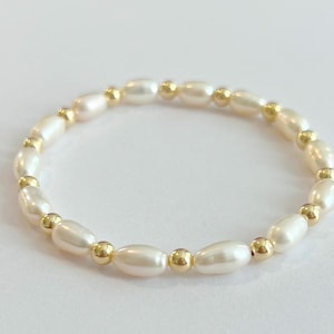 May include: A delicate bracelet made of white oval pearls and gold beads. The bracelet is simple and elegant, perfect for everyday wear.