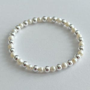 May include: A stretch bracelet featuring alternating white pearls and silver-colored beads. The bracelet is made of small, round pearls and larger, shiny silver beads, creating a classic and elegant look. This jewelry piece is suitable for everyday wear or special occasions.