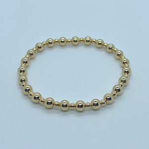 May include: A gold beaded bracelet with a simple design. The bracelet is made of small, round beads that are strung together on a thin cord.