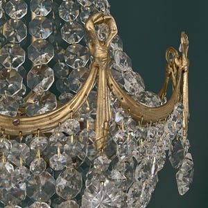 May include: Close-up of a gold-toned chandelier with numerous clear, faceted crystal pendants. The chandelier features ornate gold metalwork with curved arms and decorative accents, creating a luxurious and elegant aesthetic.