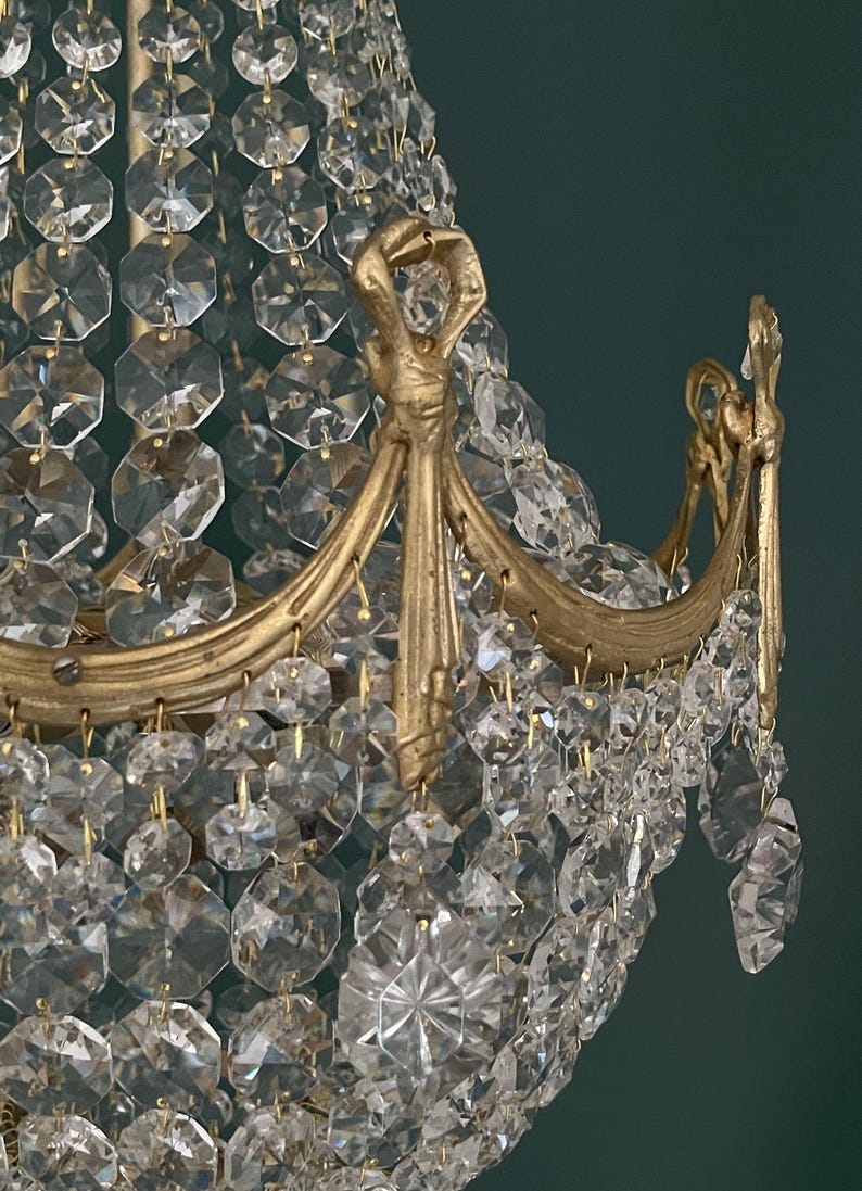 May include: Close-up of a gold-toned chandelier with numerous clear, faceted crystal pendants. The chandelier features ornate gold metalwork with curved arms and decorative accents, creating a luxurious and elegant aesthetic.