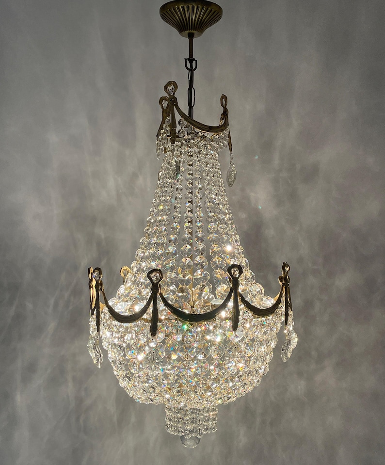 May include: A vintage chandelier with a brass frame and a cascade of sparkling crystal beads. The light fixture has multiple tiers of crystals and decorative brass accents, creating a glamorous and elegant look. The chandelier is suspended from a ceiling mount.
