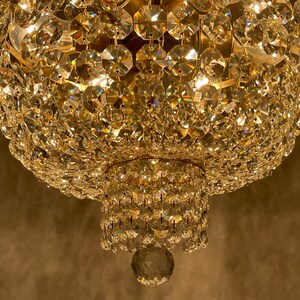 May include: Close-up of a crystal chandelier with multiple tiers of sparkling, faceted crystals. The light reflects off the crystals, creating a warm, golden glow. The chandelier is a decorative lighting fixture.