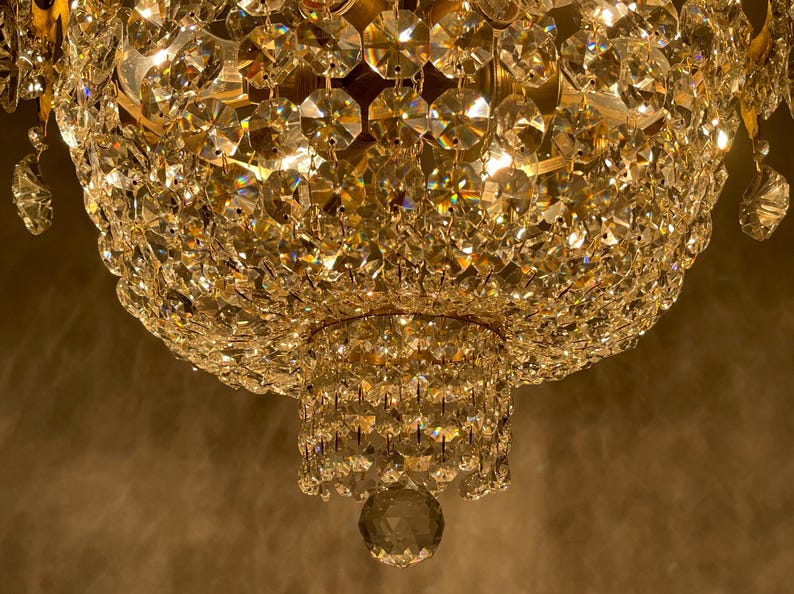 May include: Close-up of a crystal chandelier with multiple tiers of sparkling, faceted crystals. The light reflects off the crystals, creating a warm, golden glow. The chandelier is a decorative lighting fixture.