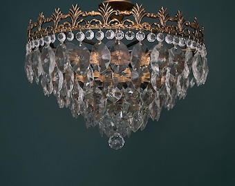 May include: An antique chandelier with a gold-colored metal frame and clear crystal pendants. The chandelier has a decorative crown-like top and multiple crystal teardrops hanging below. The crystals reflect light, creating a sparkling effect.
