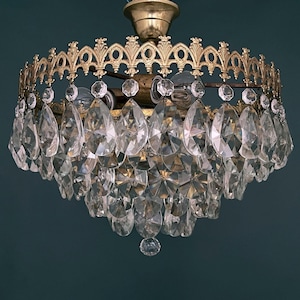 Peut inclure: Un lustre doré avec un design en cristal en forme de goutte. Le lustre a un cadre rond et orné et est suspendu à une seule chaîne.