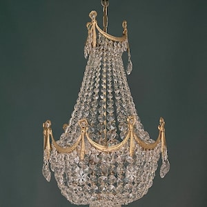 May include: An antique chandelier with a gold-colored frame and clear crystal beads. The chandelier has multiple tiers of crystals and decorative gold accents. It hangs from a matching gold ceiling mount.