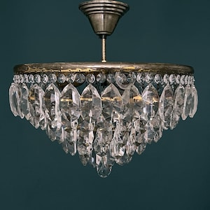 Peut inclure: Un lustre vintage en laiton et cristal avec un design rond à plusieurs niveaux. Le lustre est composé de plusieurs rangées de pendants en cristal transparent en forme de goutte.