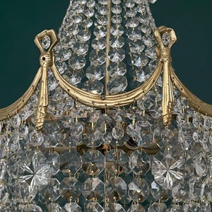 May include: Close-up of a vintage chandelier with a gold-colored frame and numerous clear crystal pendants. The crystals are faceted, reflecting light. The chandelier has an ornate design, suitable for home decor.