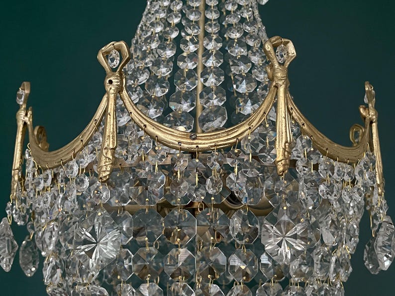 May include: Close-up of a vintage chandelier with a gold-colored frame and numerous clear crystal pendants. The crystals are faceted, reflecting light. The chandelier has an ornate design, suitable for home decor.
