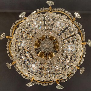 May include: Ornate chandelier with a gold-colored frame and numerous sparkling crystal pendants. The light fixture has a circular design with multiple tiers of crystals, creating a dazzling display of light and reflection.