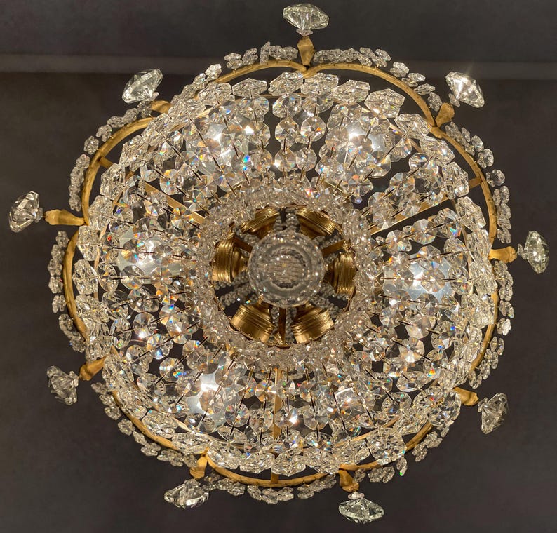 May include: Ornate chandelier with a gold-colored frame and numerous sparkling crystal pendants. The light fixture has a circular design with multiple tiers of crystals, creating a dazzling display of light and reflection.