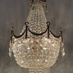 May include: An ornate chandelier with numerous crystal pendants and a brass frame. The light fixture has multiple tiers of crystals, creating a sparkling effect. The chandelier is suspended from a ceiling, showcasing its elegant design.