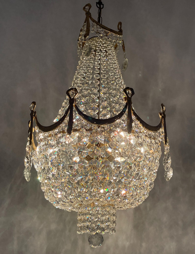 May include: An ornate chandelier with numerous crystal pendants and a brass frame. The light fixture has multiple tiers of crystals, creating a sparkling effect. The chandelier is suspended from a ceiling, showcasing its elegant design.