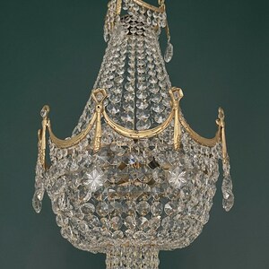 May include: An ornate chandelier with a gold-colored frame and numerous clear crystal pendants and beads. The chandelier has a tiered design with multiple layers of crystals, creating a sparkling and elegant appearance. The fixture is suspended from a chain.