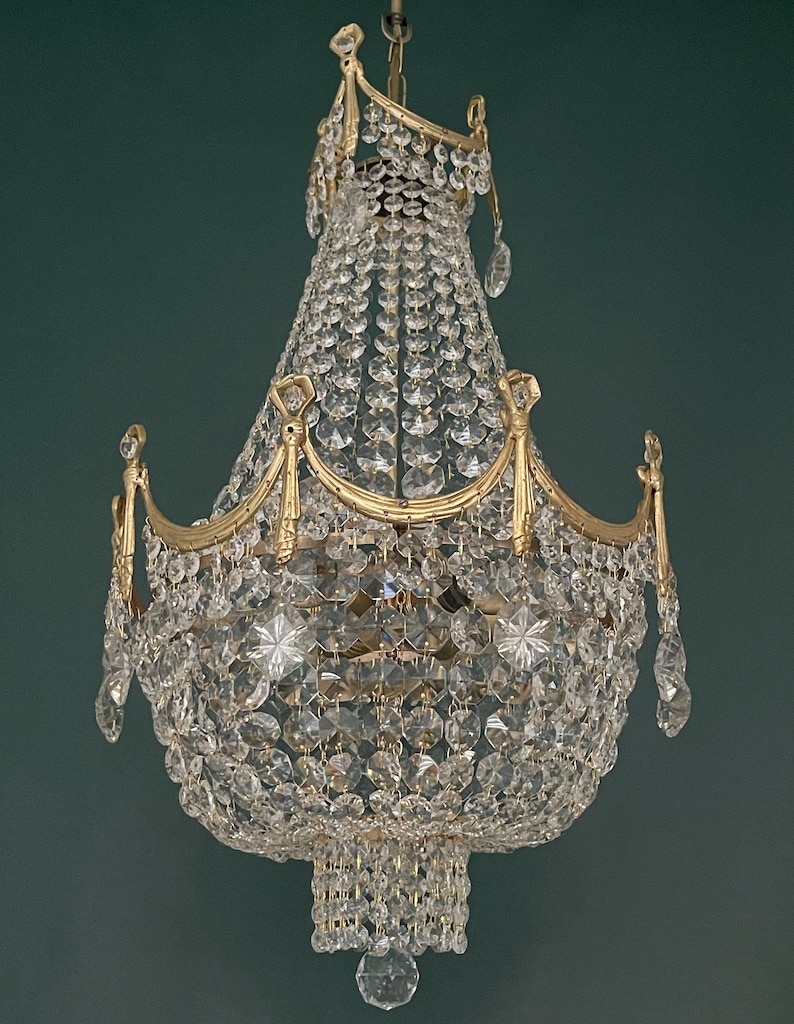 May include: An ornate chandelier with a gold-colored frame and numerous clear crystal pendants and beads. The chandelier has a tiered design with multiple layers of crystals, creating a sparkling and elegant appearance. The fixture is suspended from a chain.