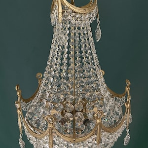 May include: A vintage chandelier with a gold-toned metal frame and cascading crystal beads and pendants. The ornate design features curved arms and decorative accents, creating a luxurious and elegant lighting fixture. The crystals reflect light, adding sparkle.